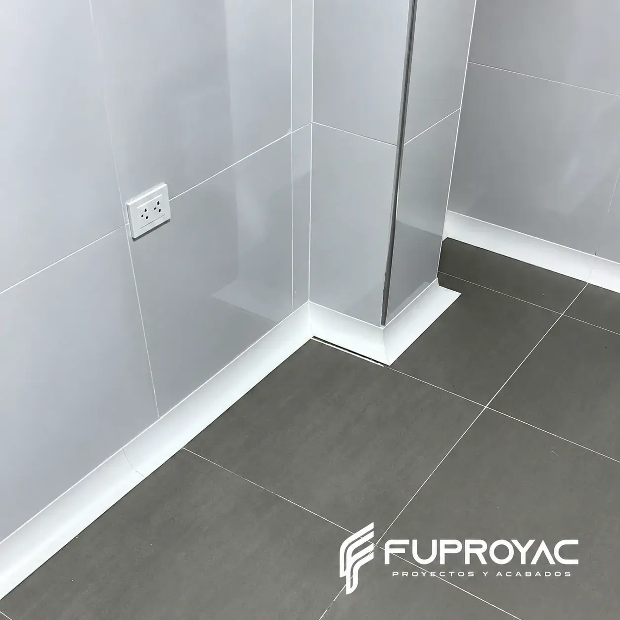 Zócalo sanitario blanco instalado en encuentro de piso gris y pared, fotografía real de FUPROYAC